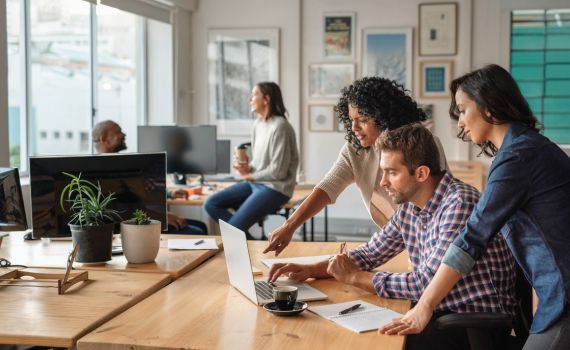 Group of people working in an office looking at a laptop together