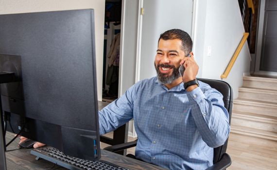 A man in a blue dress shirt talking on a phone while looking at a computer screen