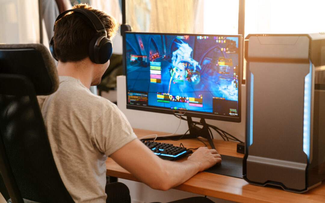 Caucasian brunette guy in headphones playing video game on his computer while sitting at home