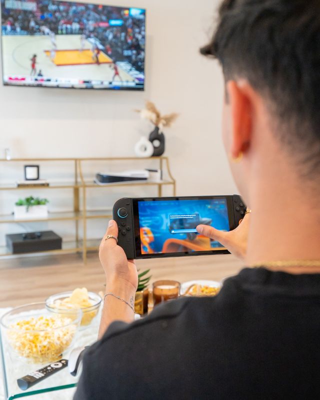 College student playing a handheld game while streaming a basketball game on TV in a Fort Collins apartment