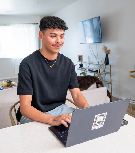 Young man sitting at a kitchen counter, smiling while working on a laptop in a bright, modern home